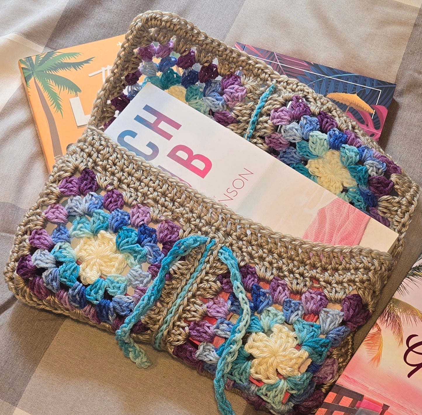Colorful crocheted clutch bag with a colorful card inside, placed on a checkered fabric background.