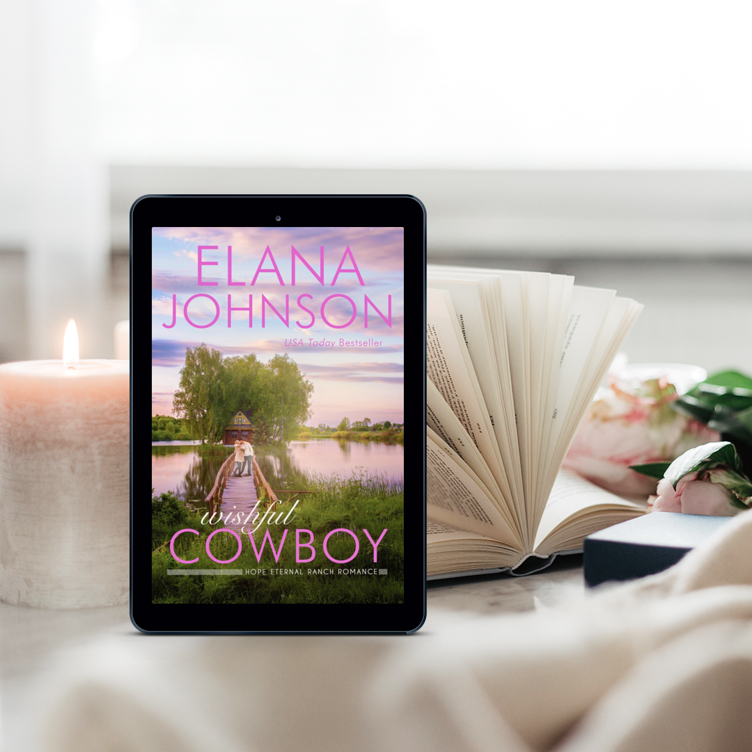 A tablet displaying Wishful Cowboy sits beside an open book and a lit candle in a soft, cozy reading setting.