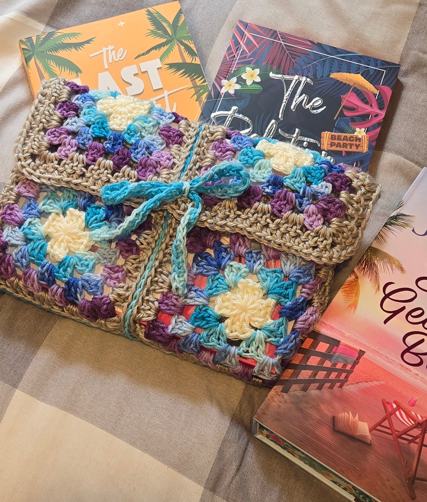 Colorful crocheted bag with a bow on a checkered surface with books in the background
