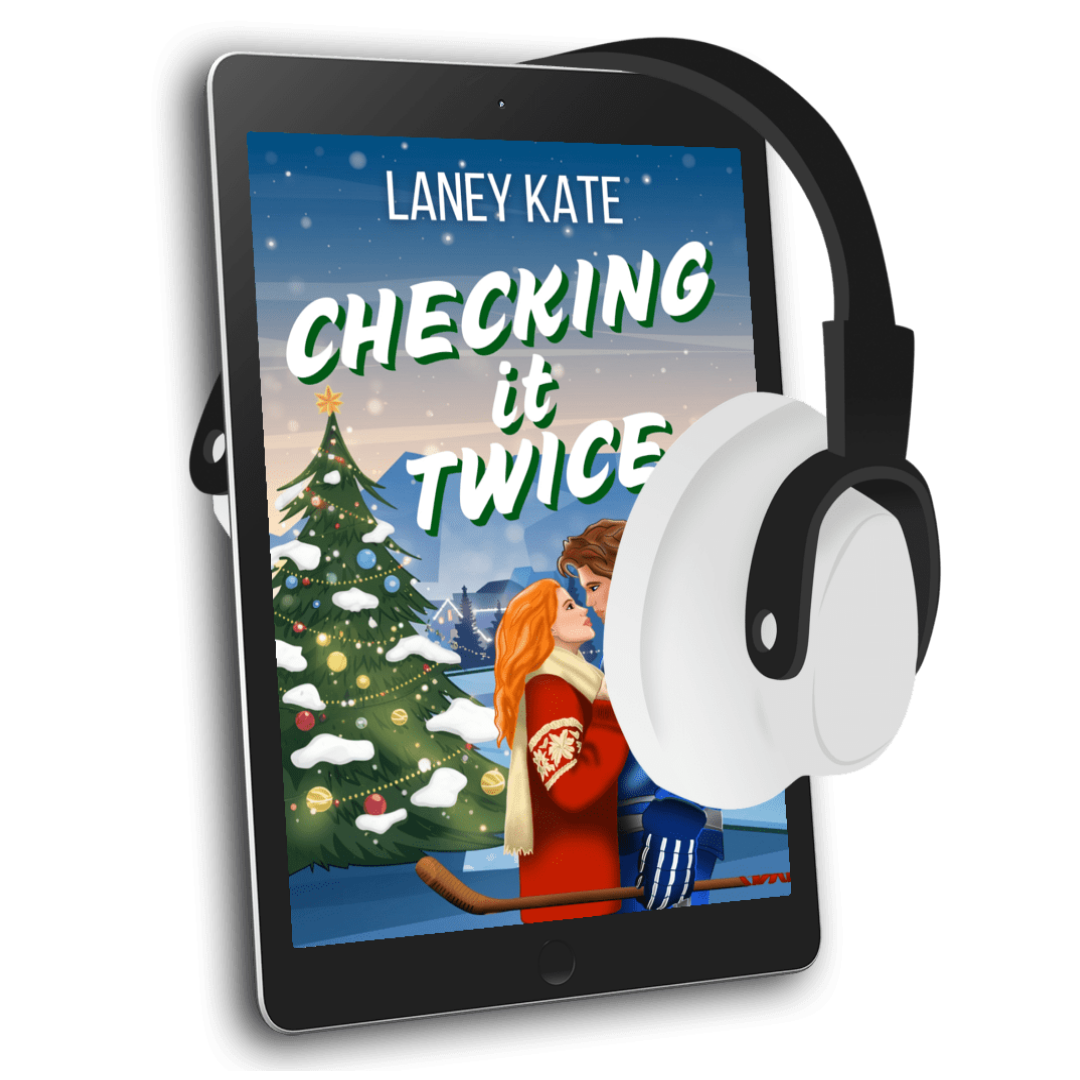 Tablet with a book cover titled 'Checking it Twice' by Laney Kate, featuring a Christmas tree and two people, with headphones on a white background.