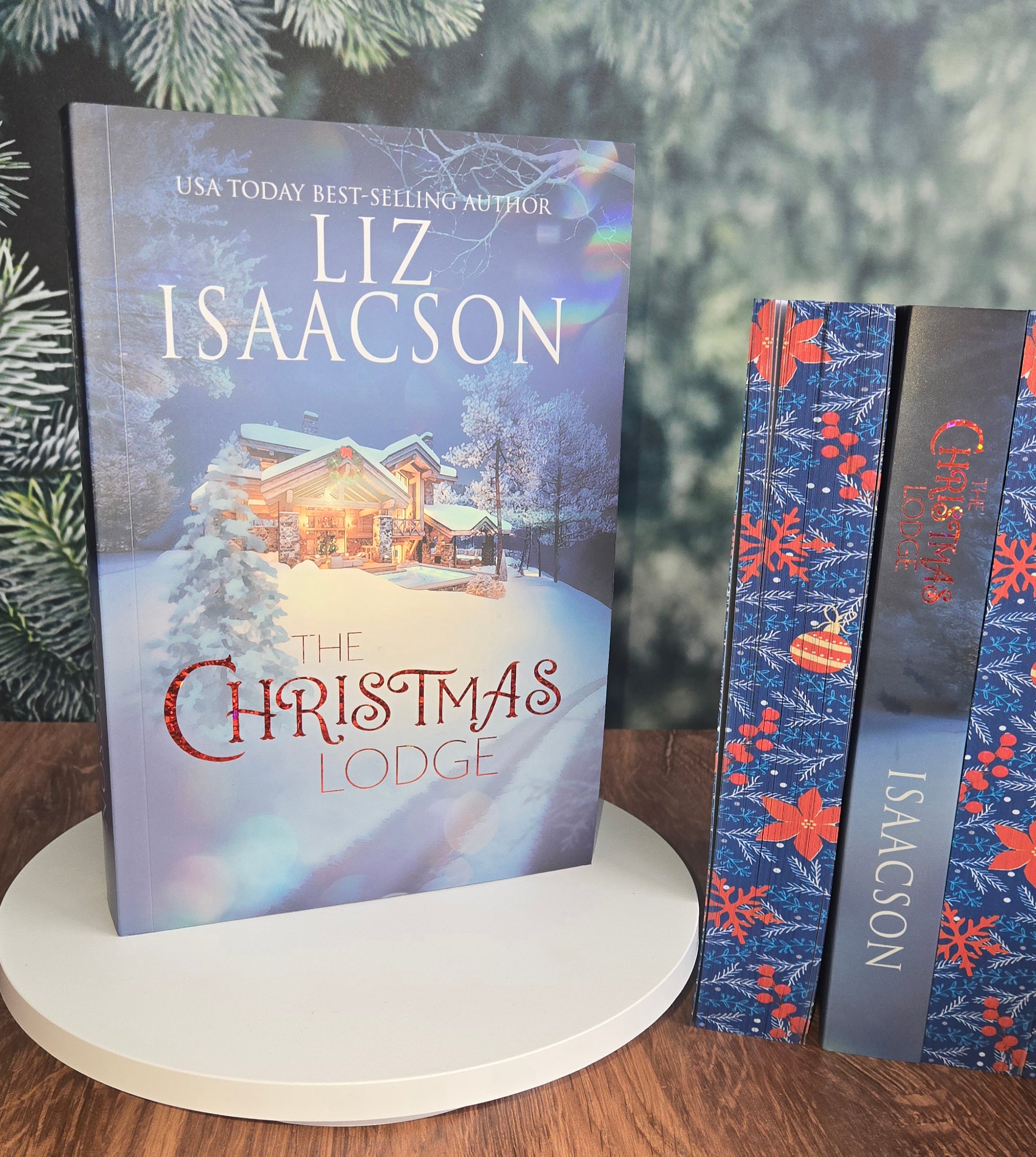 Book titled 'The Christmas Lodge' by Liz Isaacson with decorative ribbons on a wooden surface.